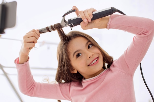 Pretty little girl curling a lock of her hair in front of the camera