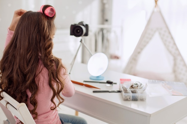 Pretty little girl curling a lock of her hair in front of the camera