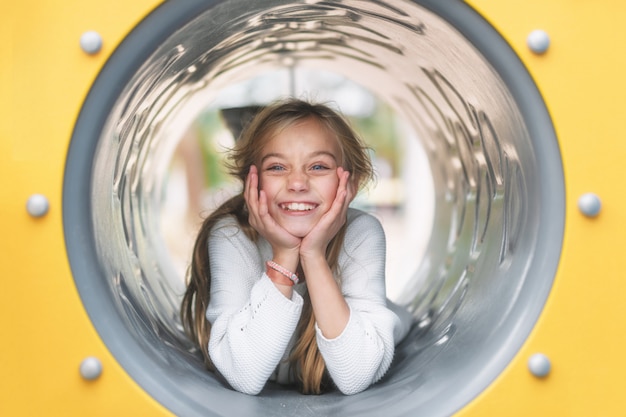 Pretty, little girl, having fun, lying on pipe on children playground.