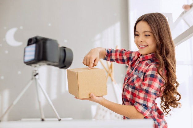 Bambina graziosa che tiene una scatola davanti alla telecamera