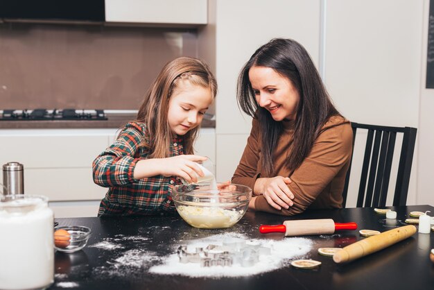 Photo pretty little girl is helping her mother with cooking.