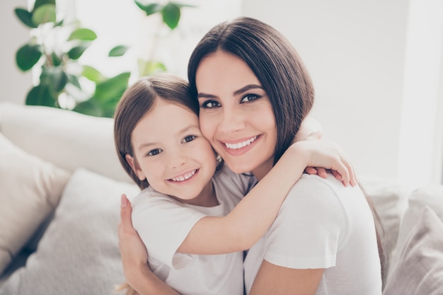 Pretty little girl leaning cheek to young mommy embracing her in home house indoors