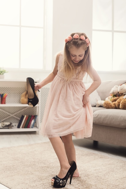 Pretty little girl in mom's shoes. Small fashionista trying on high heels at home, copy space