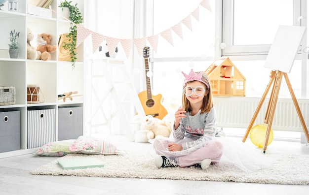 Pretty little girl playing with paper glasses in bright room