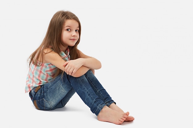 Foto bambina graziosa che si siede sul pavimento, isolato sopra bianco