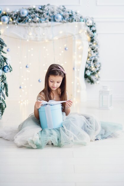 Pretty little girl sitting near Christmas tree indoors.