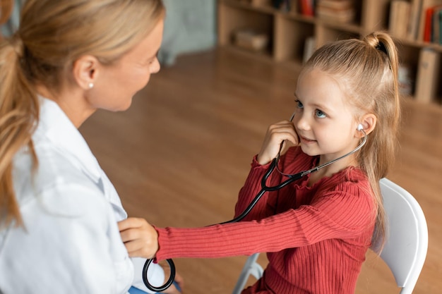 pretty little girl visiting pediatrician and playing with female doctor listening doc39s heart beating with stethoscope