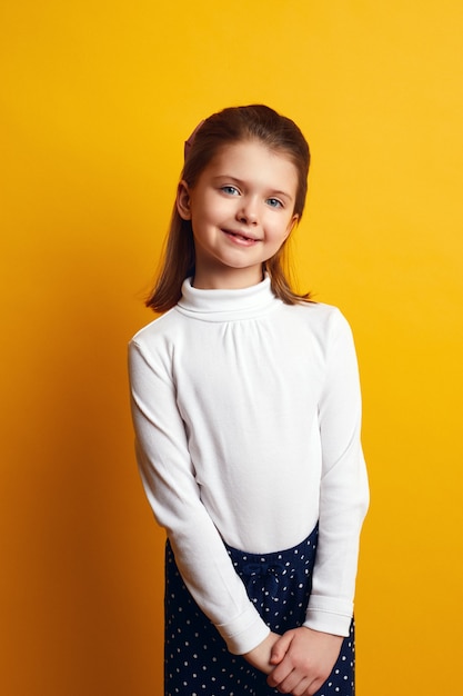 Pretty little girl in white turtleneck posing adorably on yellow background
