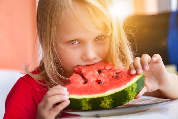 カメラを見て自宅でスイカのクローズ アップを食べるかわいい幼児の女の子 4 年