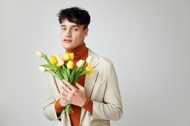 노란 꽃의 꽃다발과 함께 흰색 재킷에 예쁜 남자 우아한 스타일 모델 스튜디오