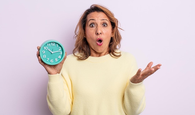 Pretty middle age woman amazed, shocked and astonished with an unbelievable surprise. alarm clock concept