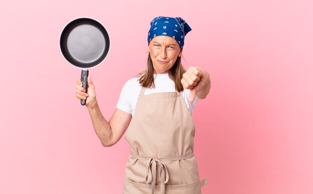 pretty middle age woman feeling cross,showing thumbs down and holding a pan. chef concept