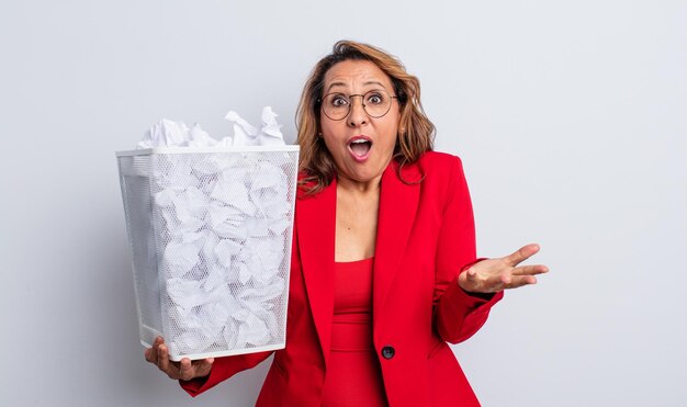 Pretty middle age woman feeling extremely shocked and surprised. paper balls bin concept