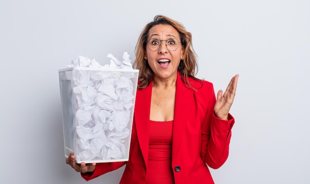 Photo pretty middle age woman feeling happy and astonished at something unbelievable. paper balls bin concept