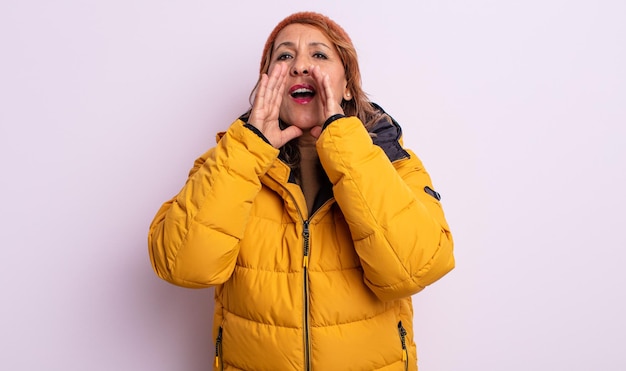 Pretty middle age woman feeling happy,giving a big shout out with hands next to mouth. winter concept