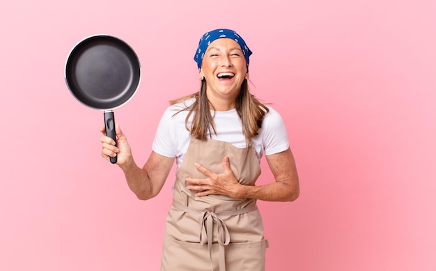 Pretty middle age woman laughing out loud at some hilarious joke and holding a pan. chef concept