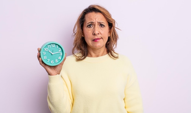 Photo pretty middle age woman looking puzzled and confused. alarm clock concept