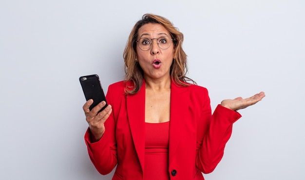 Photo pretty middle age woman looking surprised and shocked, with jaw dropped holding an object. business concept