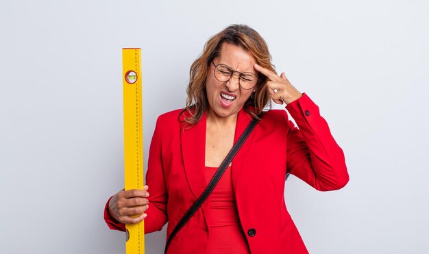 Pretty middle age woman looking unhappy and stressed suicide gesture making gun sign architect concept