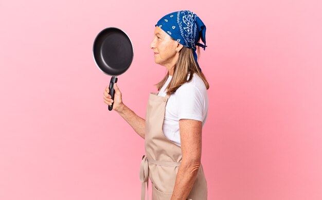 Pretty middle age woman on profile view thinking, imagining or daydreaming and holding a pan. chef concept