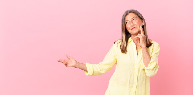 Pretty middle age woman smiling happily and daydreaming or doubting