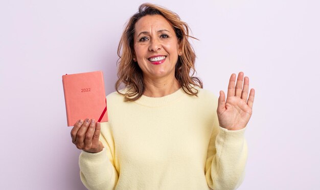 Pretty middle age woman smiling happily, waving hand, welcoming and greeting you. agenda concept