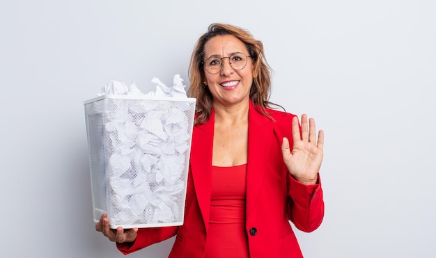 Pretty middle age woman smiling happily, waving hand, welcoming and greeting you. paper balls bin concept