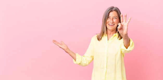 Pretty middle age woman smiling and looking friendly, showing number three