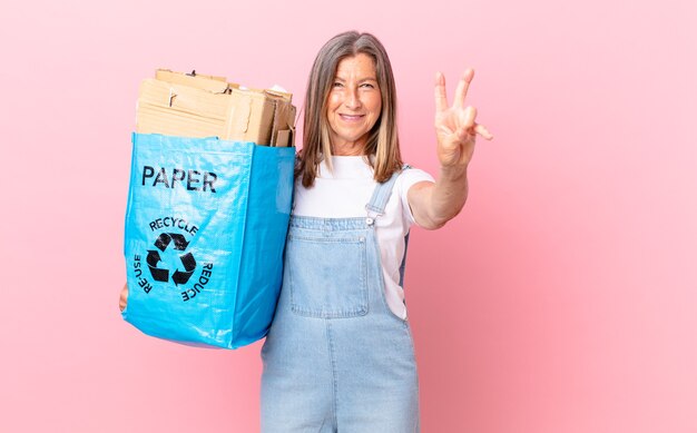 Pretty middle age woman smiling and looking happy, gesturing victory or peace recycling cardboard concept