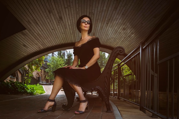 pretty middleaged woman in a black dress and hat strolls through the city park and street