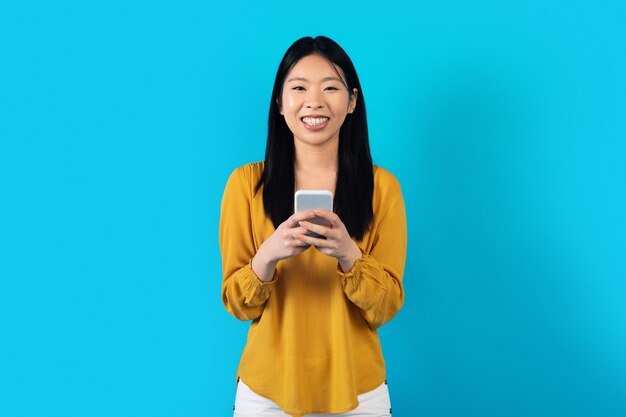 Photo pretty millennial korean woman using smartphone on blue copy space