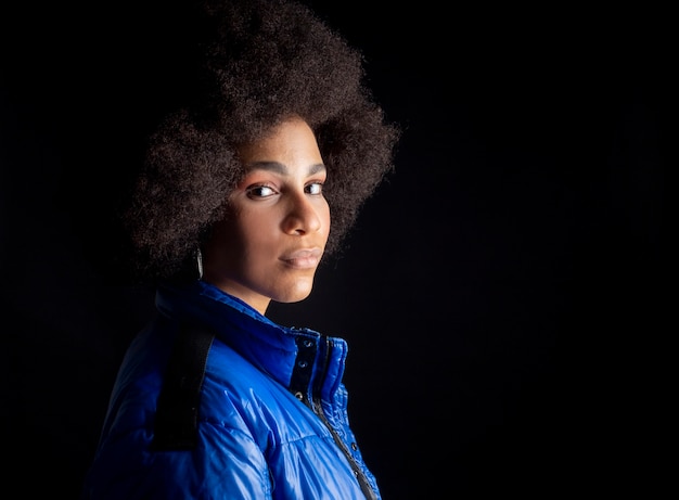 Pretty mixed afro woman, smiling, with serious urban clothes, sad look, on dark surface