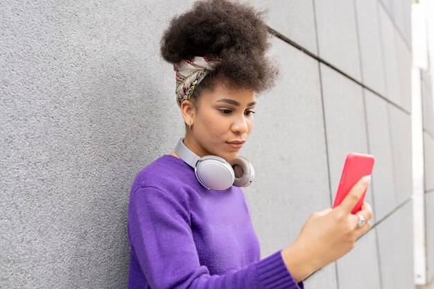 Donna di razza abbastanza mista con cuffie e smartphone per strada felice