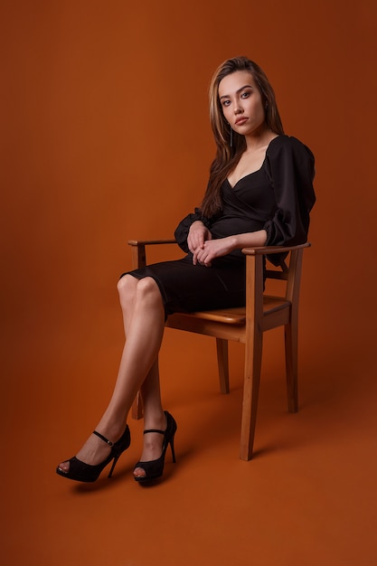 pretty model in black dress and high heels sitting in chair