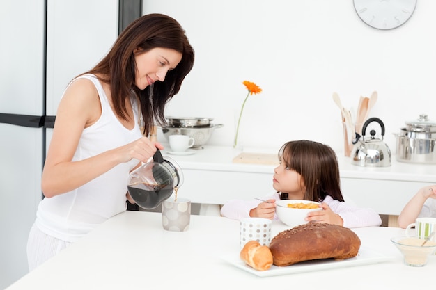 彼女の子供が朝食を食べている間に、お母さんはコーヒーを注ぐ