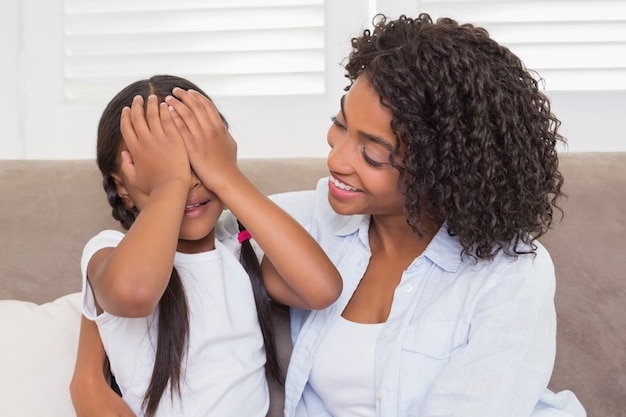 Pretty mother sitting on the couch with her daughter covering her eyes