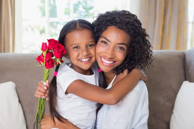 Pretty mother sitting on the couch with her daughter holding roses