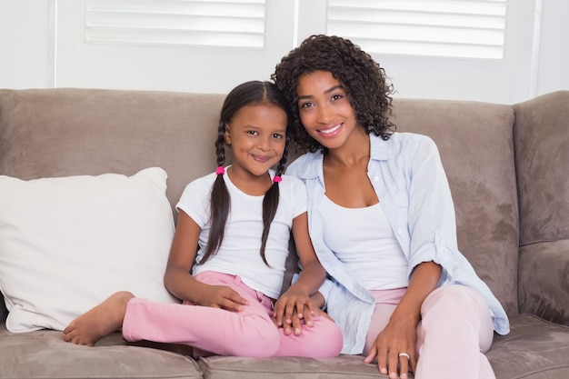 Photo pretty mother sitting on the couch with her daughter smiling at camera
