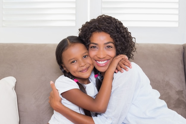 Pretty mother sitting on the couch with her daughter smiling at camera