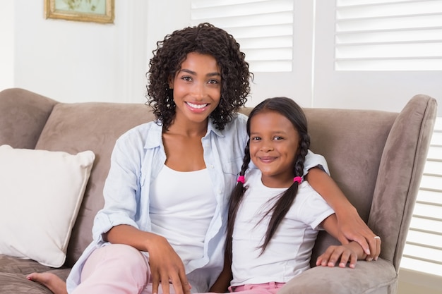 Pretty mother sitting on the couch with her daughter smiling at camera