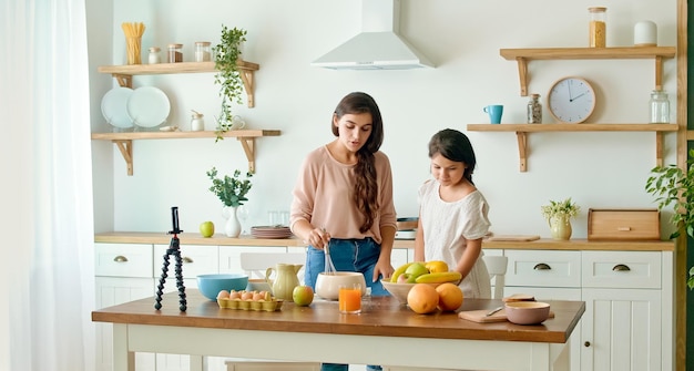 A pretty mother with a cute daughter shooting a blog about cooking video blog about healthy food a m...