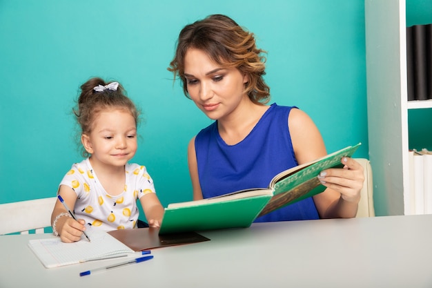 Pretty mother with cute daughter sitting with book in the room at home.