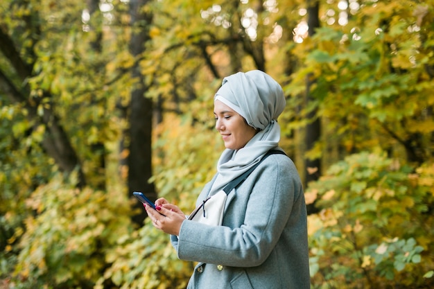 携帯電話を使用しているかなりイスラム教徒の女性スマートフォンイスラムを使用してヒジャーブを身に着けている屋外のアラビア語の女性