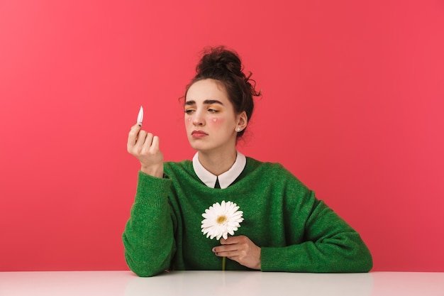 Pretty nerd girl sitting at the table isolated, holding camomile