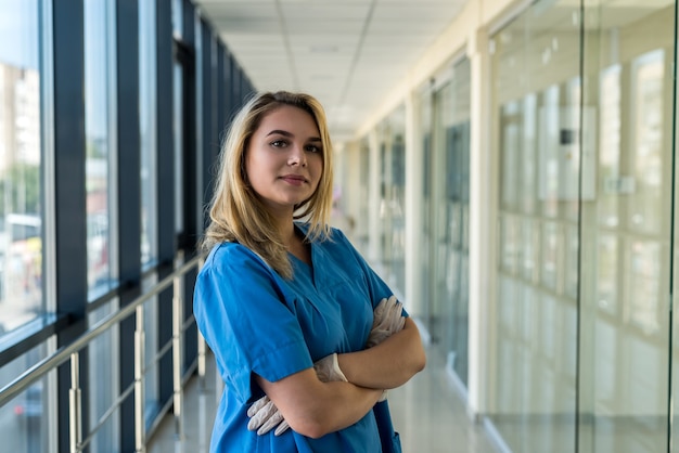 Довольно медсестра в синей форме со стетоскопом в помещении в современной клинике. Медицинский работник в больнице в ожидании диагностики пациентов