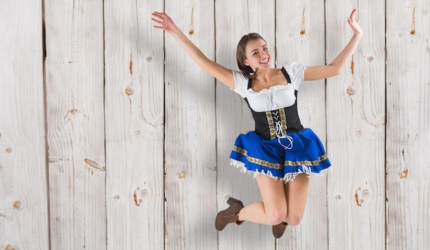 Photo pretty oktoberfest girl smiling and jumping against wooden background