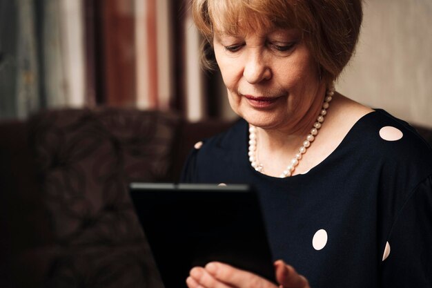 A pretty older woman uses a tablet and the Internet while sitting in the living room on a home sofa