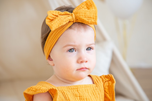 黄色い服を着たかわいい1歳の白人の女の子が床に座って目をそらします。子供の誕生日のスタジオ写真。