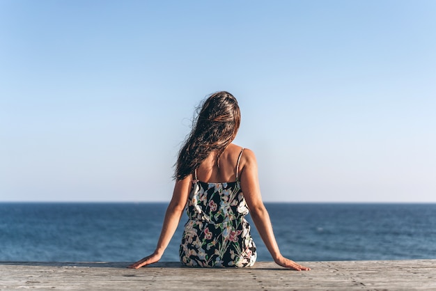 Pretty pan asian girl in dress sitting on the pier near sea.