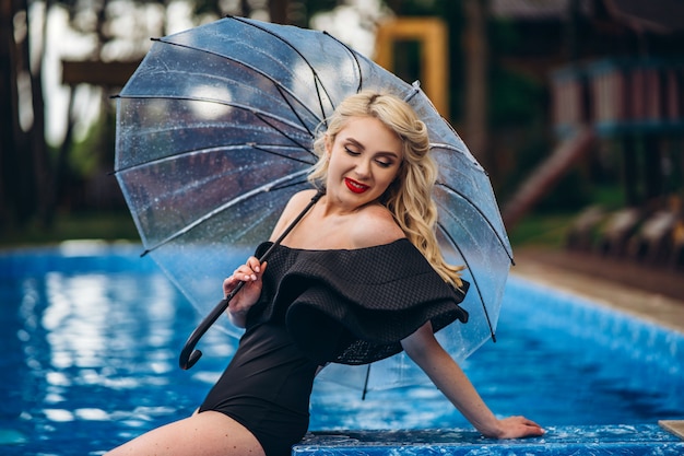 Pretty pin up styled blonde in black vintage swimsuit relaxing in the swimming pool